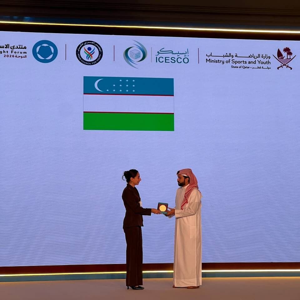 Shakhzoda Ikromova receiving a commemorative plaque from a forum representative on stage, with the flag of Uzbekistan displayed on the screen behind.